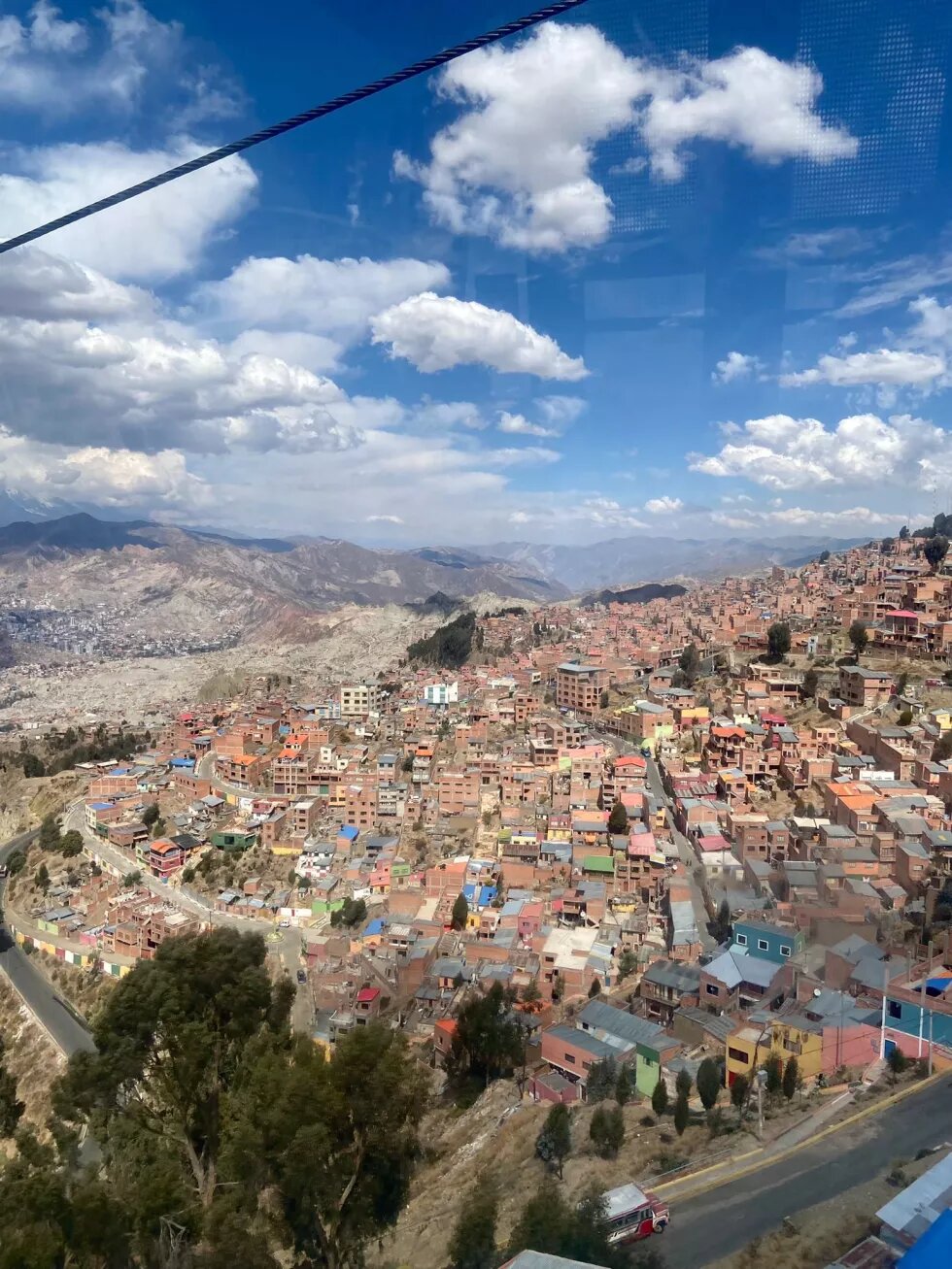 La Paz, Bolivien, von oben. Unzählige Häuser liegen an einem Hang. Am Horizont sind Berge und blauer, mit weißen Wolken durchzogener Himmel.
