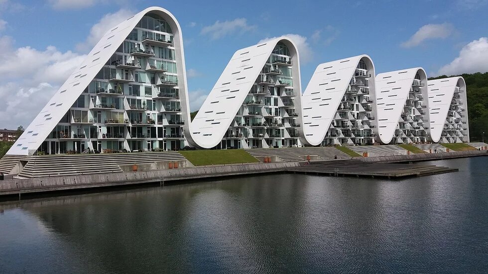 Abstrakte Bauten am Wasser in Form von Wellen. Es sind Wohn-/Bürogebäude in Vejle, eine Stadt in Dänemark.